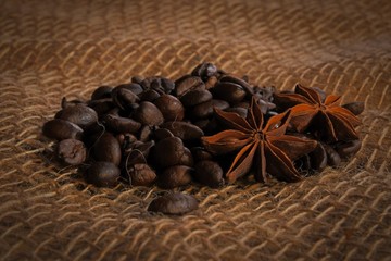 Roasted black coffee beans and anise stars on a coarse cloth