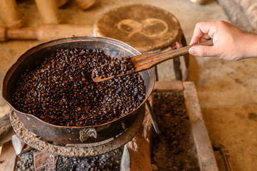 Cropped shot view of woman hill tribe hand trying to roasting coffee beans by traditional local ways, using metal pot and wooden spatula. Roasting brings out the aroma and flavor inside coffee beans.