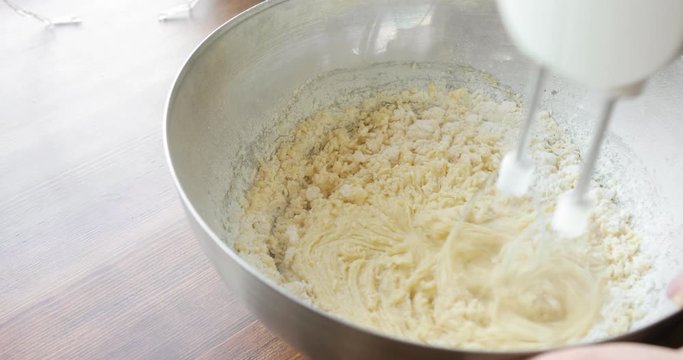 Baker mixing ingredients in bowl cooking dough baking cake using electric mixer, closeup view. Steps of baking and confectionery. Preparing sweet food dessert in kitchen at home on wooden table.
