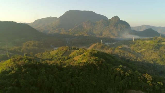 Aerial shot of idyllic green landscape during sunrise, drone flying forward over forest against sky - Tat Sae Waterfalls, Laos