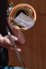 A face mask on the bell of a trombone that is being played by an orchestra musician