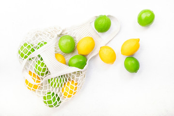 Organic lemons and limes in reusable eco-friendly string mesh bag. Zero waste, plastic free and sustainable lifestyle concept. White kitchen table background, copy space, top view