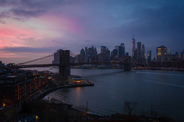Fototapeta na wymiar New York City, USA - 26 Dec 2019: Dramatic, colorful Sunset at the East River with Manhattan Skyline Lights and Brooklyn Bridge