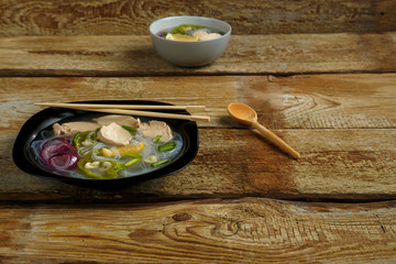 Black plate of Vietnamese Pho soup with chicken on a wooden table and appliances.