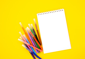 multi-colored markers with a white blank Notepad on a yellow background, space for text