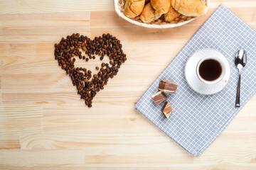 A cup of coffee on a napkin on a wooden table and a scattered jaundice of coffee in the shape of a heart.