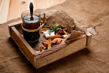 Fototapeta na wymiar Tea in a glass cup with a cup holder, served in a rustic style, shot on a wooden surface, coated with a rough cloth. Background for traditional hot drinks.
