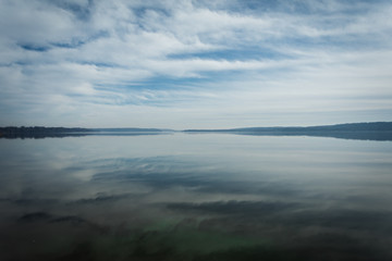 Fototapeta premium Reflections of Clouds in the Sky on calm, tranquil Water with Trees on Horizon and plenty of Copy Space