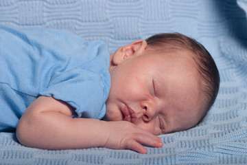 Infant baby boy sleeping on a blue blanket