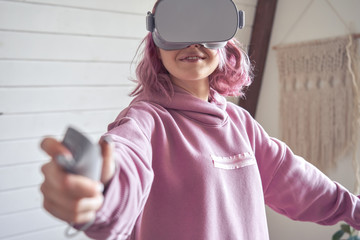 Teen girl wear vr goggles hold controller playing virtual reality video game using digital innovation headset app. Young adult woman gamer pink hair play 360 3d videogame immersive simulator at home.