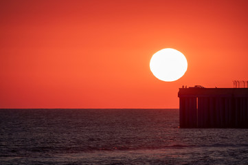 Beautiful red and orange sunset over the sea. The sun goes down over the sea. Silhouette of a pier with fishermen at sunset