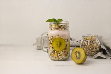 Homemade granola witn kiwi in open glass jar on white wooden background