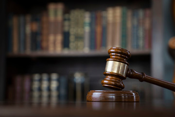 Judge office. Gavel on brown shining table and collection of legal books in the bookshelf.
