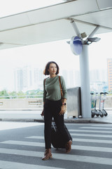 Beautiful woman happily walking along pedestrian strip with suitcase and airport on background