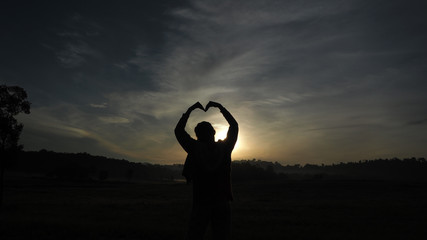 A woman standing facing the sun Looking at a wide field, heart-shaped arms, sun light shining through the model.