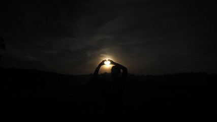 A woman standing facing the sun Looking at the wide field, heart-shaped hand-made, the light of the sun shining through the model.