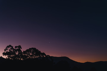 sunset sky with blue to purple to orange gradient colors (unedited) and moon over the hills with eucalyptus tree silhouettes