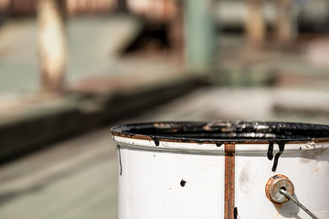 weißer geöffneter Metalleimer mit schwarzer Farbe vor unscharfem Hintergrund
