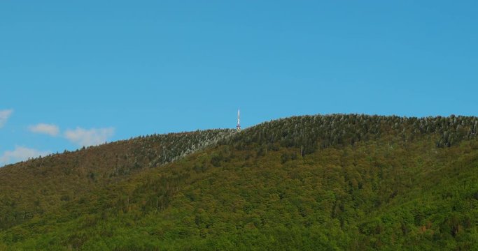 Slide right move on Radhost Pustevny hill with signal transmitter on top view from below during a sunny day with clouds.