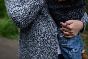 mother in a dark blue knitted sweater holds a child in jeans in her hands walking through the...