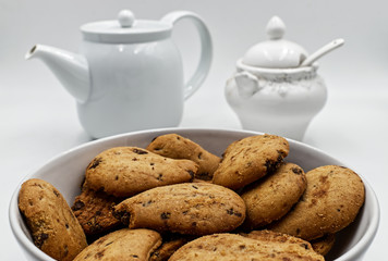 Dry tea biscuits with teapot and sugar bowl on white background