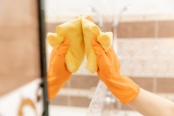 Woman cleans mirror from pollution and plaque from water in bathroom