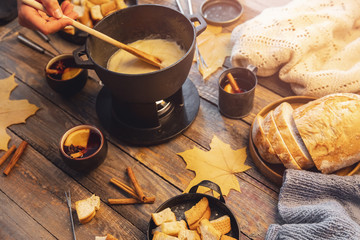 Girl cooks gourmet Swiss fondue dinner with cheese on fire, autumn wooden background with maple leaves. Top view, flat lay