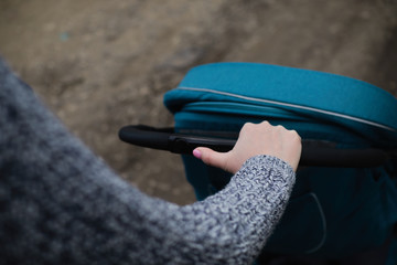 Young woman walking a coach outdoor. Closeup shot of female hands with a black stroller handle. Mother pushes a stroller around the city. The concept of active and healthy education.