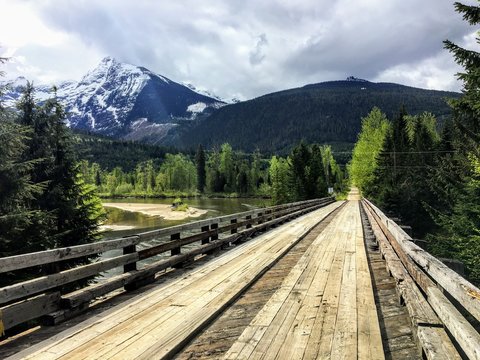 a wooden bridge with the mountains and forest in the background