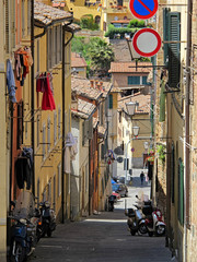 A classic Italian street view, which includes generic apartment buildings with clothes drying outside and scooters parked below, is shown in a vertical view during the day.
