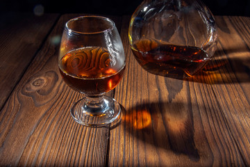 Pouring brandy or cognac from a bottle into a glass on a wooden old table.