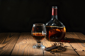 Pour cognac or brandy into a large glass on an old rustic table. Vintage wooden background, night mood. Place for text, dark background, selective focus.