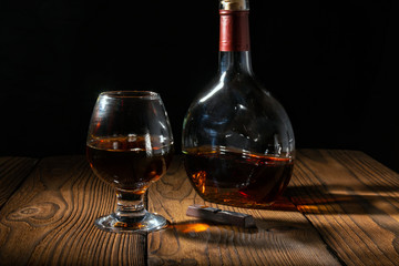Pour cognac or brandy into a large glass on an old rustic table. Vintage wooden background, night...