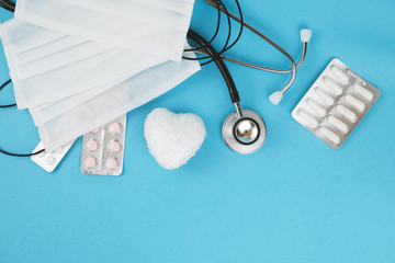 Medical stethoscope, white heart, pills, masks on blue background.Top view.Place for a text.