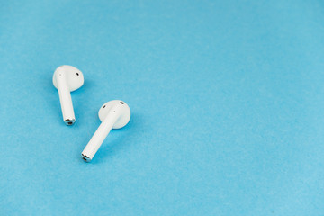 Wireless white headphones on blue background. Place for a text.