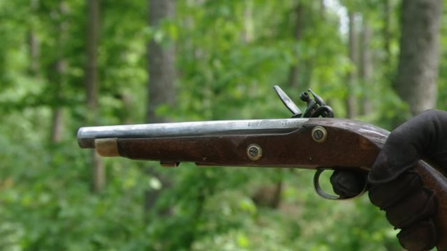 Gloved hand squeezes trigger to fire old flintlock pistol, close-up