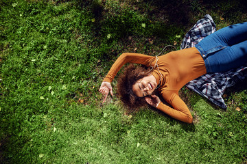 Top view of mixed race woman lying down on the lawn, enjoying music on a beautiful sunny day.