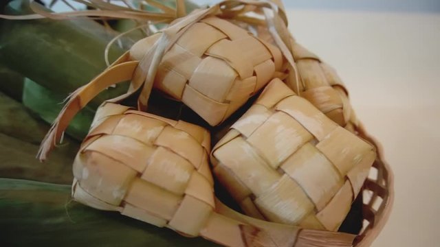Cinematic shot of popular Malay traditional food, Ketupat rice and Lontong Nasi Impit in one basket. Ketupats, a natural rice casing made from young coconut leaves for cooking rice. Slow motion video.