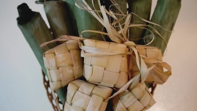 Cinematic shot of popular Malay traditional food, Ketupat rice and Lontong Nasi Impit in one basket. Ketupats, a natural rice casing made from young coconut leaves for cooking rice. Slow motion video.