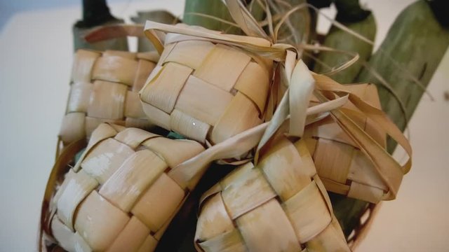 Cinematic shot of popular Malay traditional food, Ketupat rice and Lontong Nasi Impit in one basket. Ketupats, a natural rice casing made from young coconut leaves for cooking rice. Slow motion video.