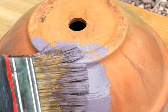 Person painting a terracotta flower plant pot purple,  with a paint brush.  Restoration upcycle concept
