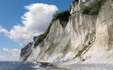 The high and impressive chalk cliffs of the Danish island of Mon in the Baltic Sea. The rocks are over 100 meters high. On the left are the waves of the Baltic Sea with sunshine and a blue sky.