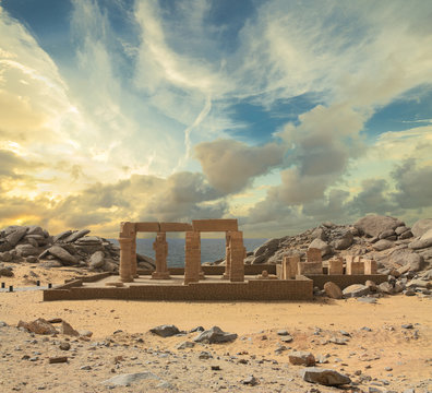 A ruin with columns next to the historic Kalabsha Temple on an island in Upper Egypt in the late afternoon. There are dramatic clouds in the sky. In the background is the lake.