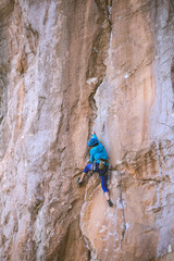A woman in a helmet climbs a beautiful orange rock.
