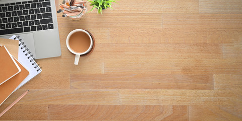 Top view wooden office desk with coffee, computer laptop, note, pencils, pencil holder, potted...