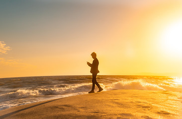 Fototapeta na wymiar 日本 神奈川県 鎌倉の七里ヶ浜の砂浜を夕方に歩く若い日本人男性と美しい夕陽