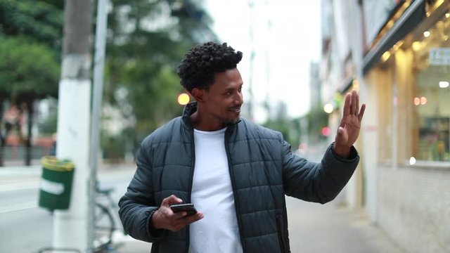 Charismatic mixed race man waving hello to person in street, black guy walking in sidewalk waves HI
