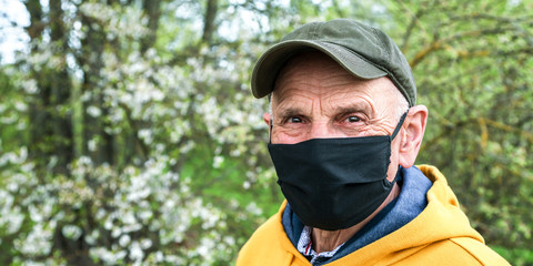 senior man in cap black mask looks ahead in garden closeup