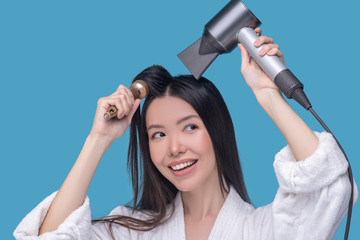 Brunette young asian woman drying her hair and smiling
