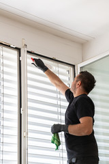 professional cleaner cleaning window blinds in an apartment with a green micro fiber cloth